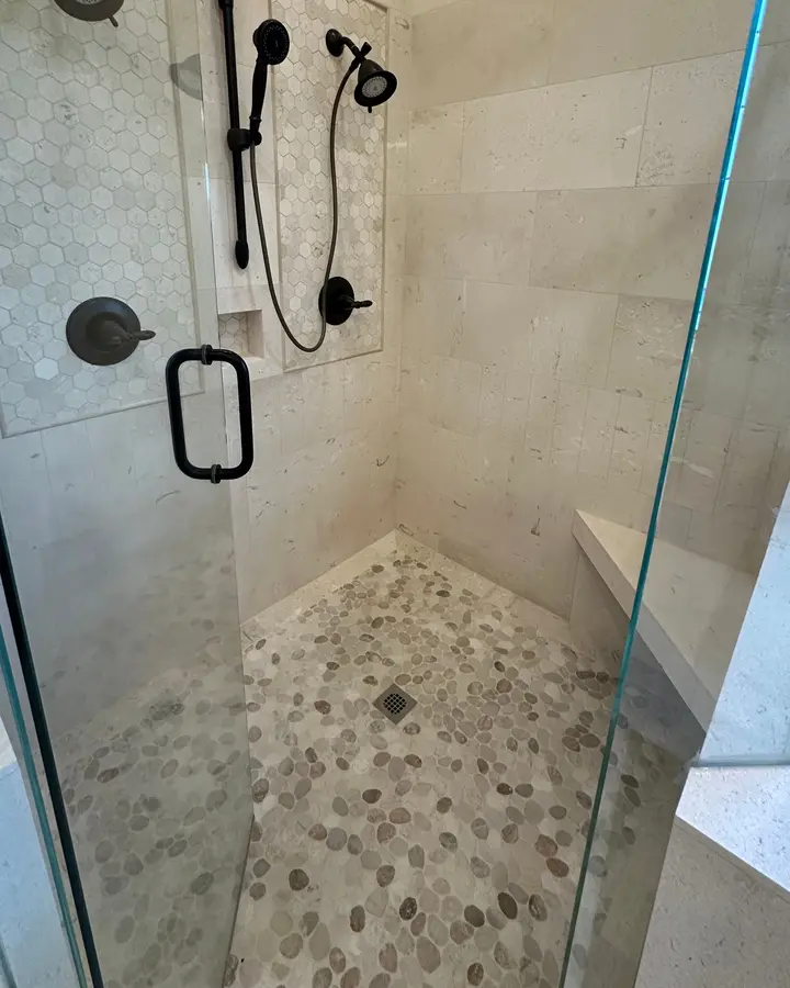Ducha de piedra caliza con piso de guijarro y banca de mosaico, instalada por B & B Pro Tile